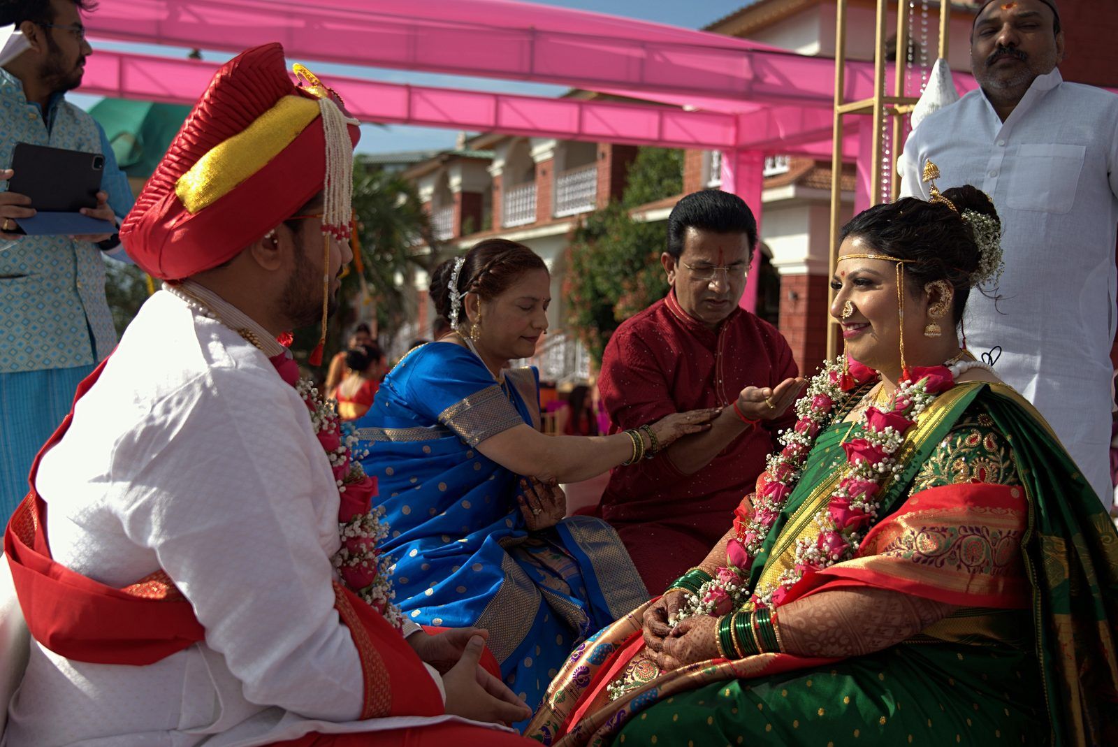 A sample straight out of the pipeline, in ceremony order: arrival at the resort, a bouquet held in mehndi-decorated hands from Seemant Poojan, a Haldi portrait of the groom in a yellow kurta beside a flowering hedge, Lagna Vidhi, the bride's entry at Mangalashtak, the Varat shot from the drone, reception portraits (photographer-graded passthrough), and a Sangeet stage performance under the adaptive-gamma night grade.
